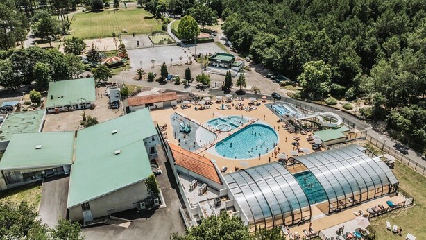 An aerial view of a resort with multiple swimming pools, a large covered area, and a surrounding forested landscape. - ZEcamping piscine couverte dog friendly animations locatif LV BBQ (Léon)