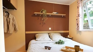 Ein ordentlich bezogenes Bett mit weißen Leinen, eine Sonnenbrille, ein Tablett mit einer Tasse und Keksen sowie eine hängende Pflanze auf einem Regal über dem Bett.