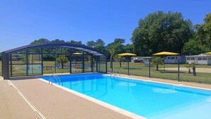 Ein Pool mit Glaskuppel, umgeben von einem Zaun und gelben Sonnenschirmen.