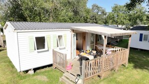 A mobile home with a deck area featuring a table and chairs, a small seating area, and a pink flamingo decoration. - ZEcamping 3* piscine animaux acceptés fitness locatif 45m2 6 pers (Vensac)