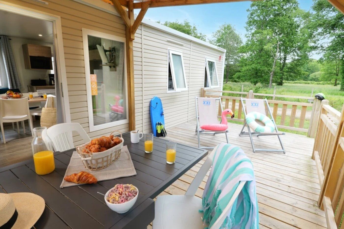 Eine überdachte Terrasse im Freien mit einem für das Frühstück gedeckten Tisch, darunter Croissants und Orangensaft, sowie zwei Liegestühlen.