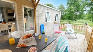 A covered outdoor deck with a table set for breakfast, including croissants and orange juice, and two lounge chairs.