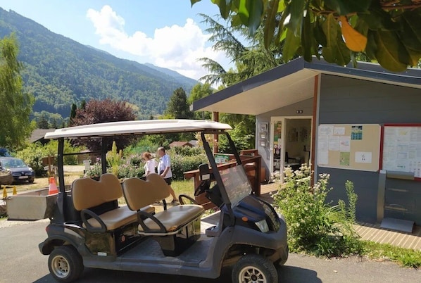 A golf cart parked in front of a building with a covered area and a bulletin board with notices.