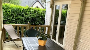 Een overdekt terras met een tafel en stoelen, een potplant en uitzicht op een huis en groen in de verte.