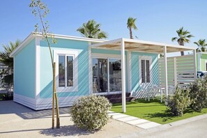 A small, single-story building with a light blue exterior, a covered porch with white furniture, and a well-maintained lawn.