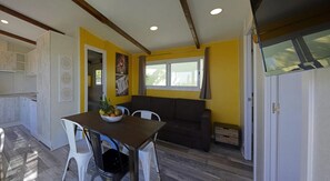 A compact living space with a kitchenette, a dining area with a table and chairs, a sofa, and a window providing natural light.