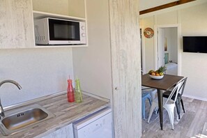 A compact kitchen with a microwave, a sink, and a dishwasher. There is a dining area with a table and chairs, and a fruit bowl on the table.