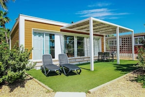 A modern house with a covered patio, two lounge chairs, and a small garden.