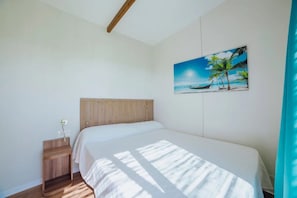 A bedroom with a wooden headboard, a single bed, a nightstand, and a wall-mounted painting of a beach scene.