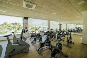Ein Fitnessraum mit Cardiogeräten, großen Fenstern und Blick auf Palmen.