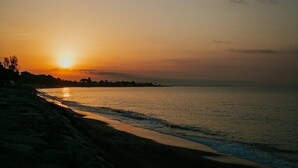 Un atardecer sobre un mar tranquilo, con una playa y una costa lejana.