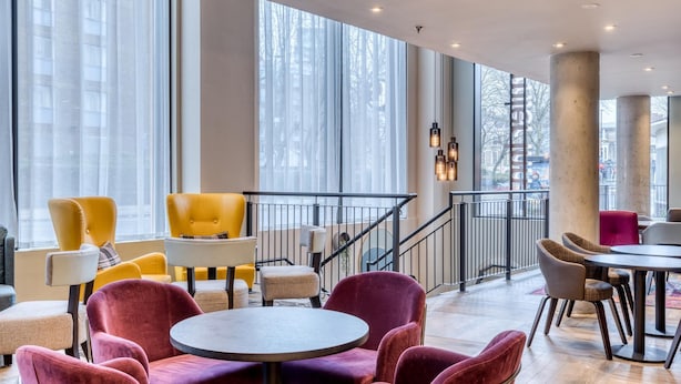 A modern interior with yellow and purple chairs, a staircase, and large windows. - Premier Inn London Waterloo - Lambeth Road (London)