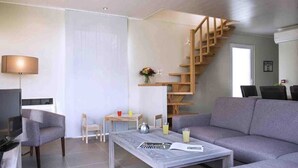 A modern living room with a grey sofa, a coffee table, a TV, a lamp, a small table with drinks, and a wooden staircase.