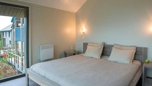 Een slaapkamer met een groot bed, een nachtkastje, een wandlamp en een raam met uitzicht op een balkon.