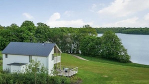 Een herenhuis met een balkon dat uitkijkt over een meer, omringd door groen.