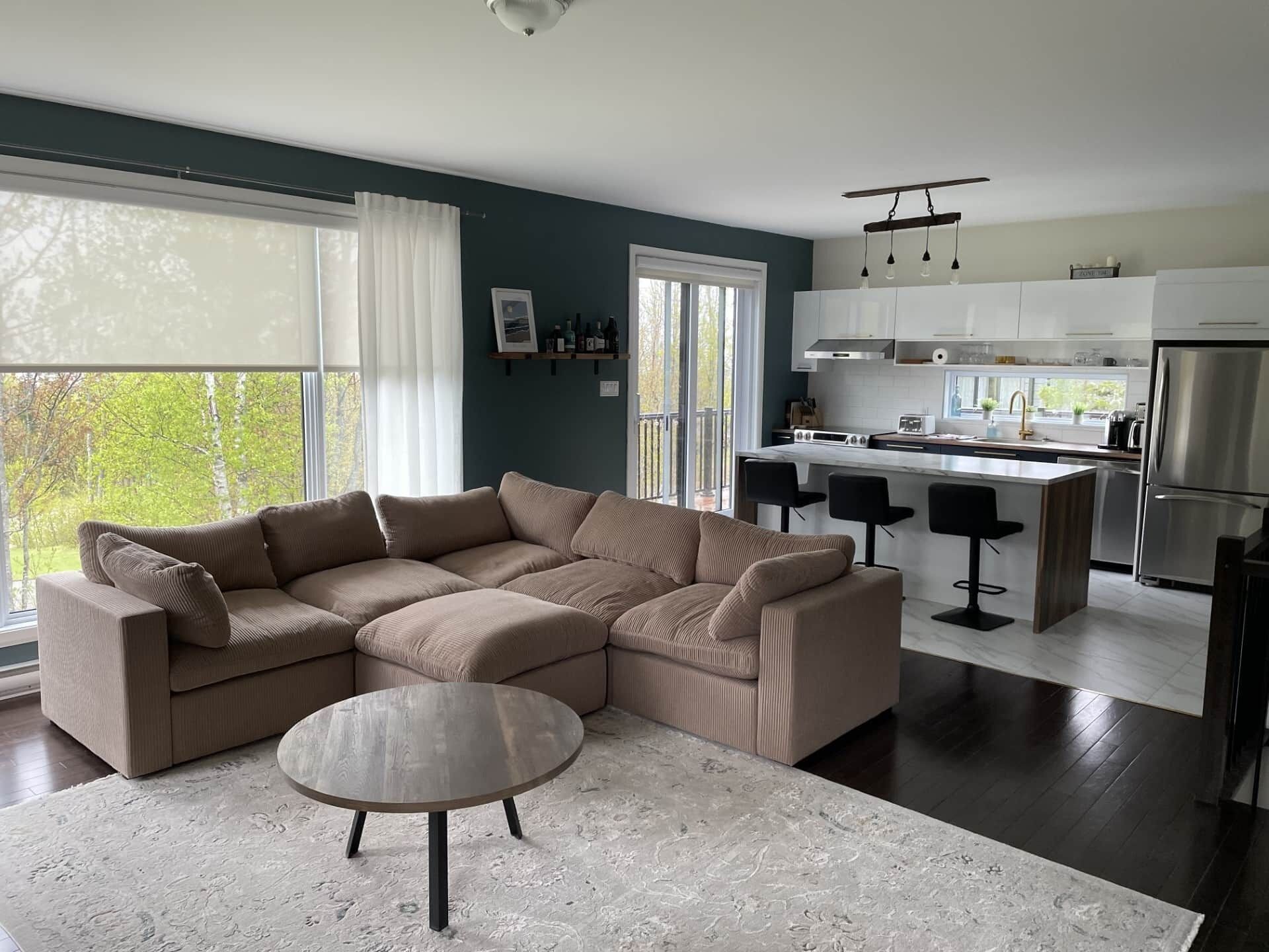 A modern living room with a sectional sofa, a round coffee table, and a kitchen area with a bar and a refrigerator.