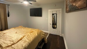 Une chambre à coucher avec un lit, un ventilateur de plafond, une porte avec un miroir et un tableau accroché au mur.