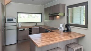 A modern kitchen with a wooden island, bar stools, a microwave, a coffee maker, and a window with blinds. - ZEcamping 4* animé locatif TV LV clim 130m2 8 pers (Froidchapelle)
