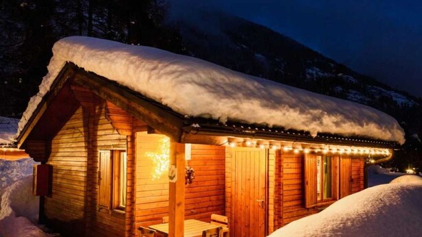 A wooden cabin with a snow-covered roof, a porch with a bench, and string lights. - ZEcamping 2* animations locatif TV 40m2 5 pers (Fucine)