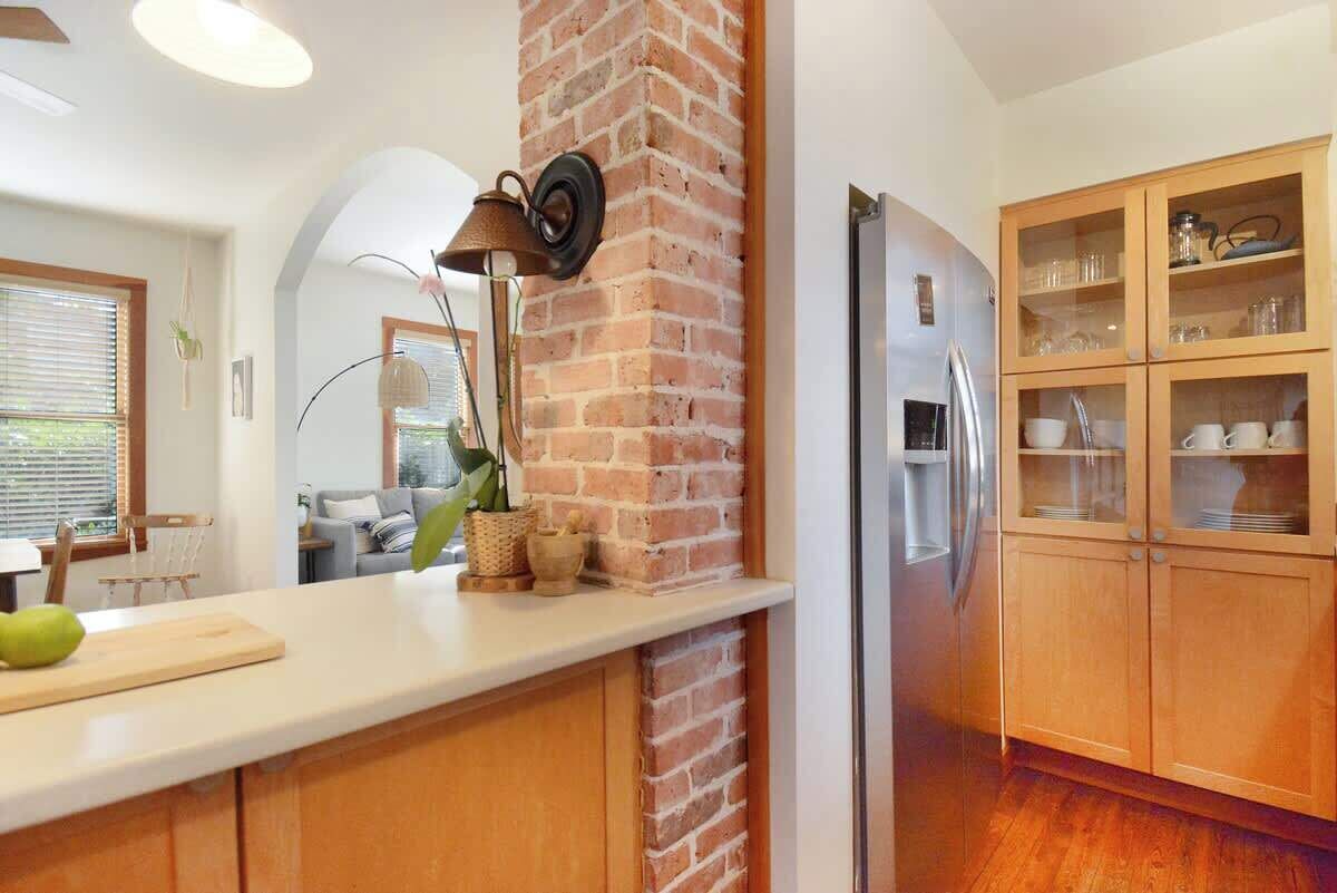 Cucina con colonna in mattoni, mobili in legno, frigorifero in acciaio inossidabile e piano di lavoro bianco.