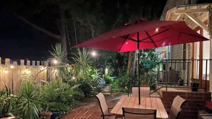An outdoor patio area with a wooden table and chairs, a red umbrella, and potted plants. - Downton Abbottry 2/2 - 5 Min Walk To City Gates (St. Augustine)