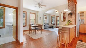 A spacious kitchen with wooden flooring, a dining area with a table and chairs, a bar area with stools, and a living room with a sofa and a coffee table. - Downton Abbottry 2/2 - 5 Min Walk To City Gates (St. Augustine)