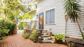 A white house with a brick pathway leading to a front door, surrounded by greenery and a bench. - Lil’ Abbottry - 1/1 Apt - 5 Min Walk to City Gates (St. Augustine)