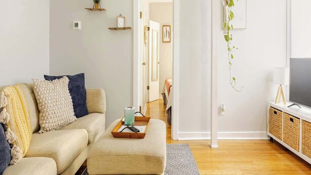 A modern living room with a sofa, ottoman, and a TV stand. - Lil’ Abbottry - 1/1 Apt - 5 Min Walk to City Gates (St. Augustine)