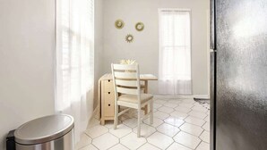 A room with a wooden desk, a chair, and a trash bin. There are two wall decorations and a window with curtains. - Lil’ Abbottry - 1/1 Apt - 5 Min Walk to City Gates (St. Augustine)
