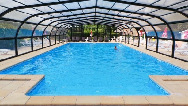A covered swimming pool with clear blue water, surrounded by lounge chairs and umbrellas.