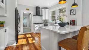 Une cuisine moderne avec des meubles blancs, un îlot central, des luminaires suspendus et un plancher en bois.