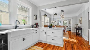 Une cuisine moderne avec des meubles blancs, un plancher en bois et des luminaires suspendus.