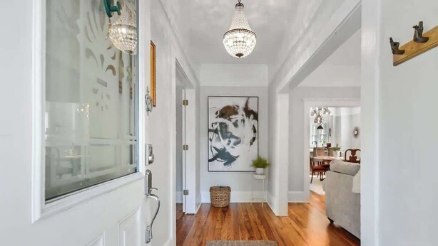 Un couloir doté d’un parquet en bois, d’un lustre et d’un tableau abstrait encadré accroché au mur.
