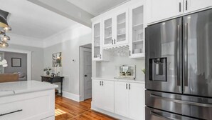 Une cuisine moderne avec des meubles blancs, un réfrigérateur en acier inoxydable et un plancher en bois.