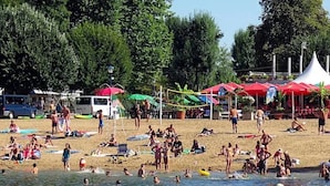 Una playa con gente tomando el sol, nadando, tiendas de campaña y un bote en el agua.