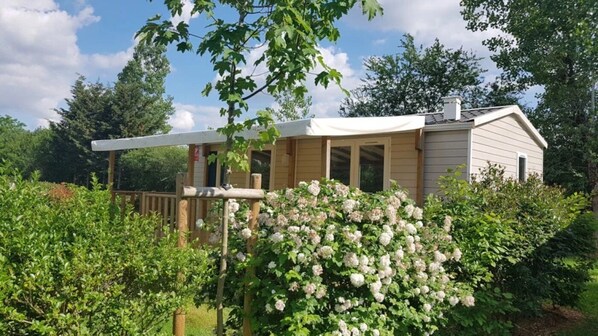 A single-story house with a covered porch, surrounded by lush greenery and flowering bushes.