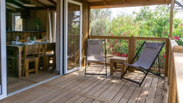 A wooden deck with a dining area and two lounge chairs.