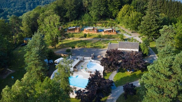 An aerial view of a resort with multiple cabins, a swimming pool, and a forested backdrop. - ZEcamping 3 étoiles pataugeoire piscine chiens acceptés locatif LV (Le Bez)