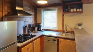 A kitchen with wooden cabinets, a stove, a sink, and a window with blinds. - ZEcamping 3 étoiles pataugeoire piscine chiens acceptés locatif LV (Le Bez)