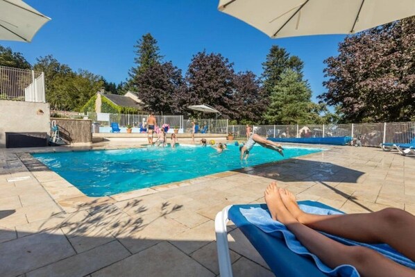 A swimming pool area with a tiled deck, lounge chairs, and umbrellas.