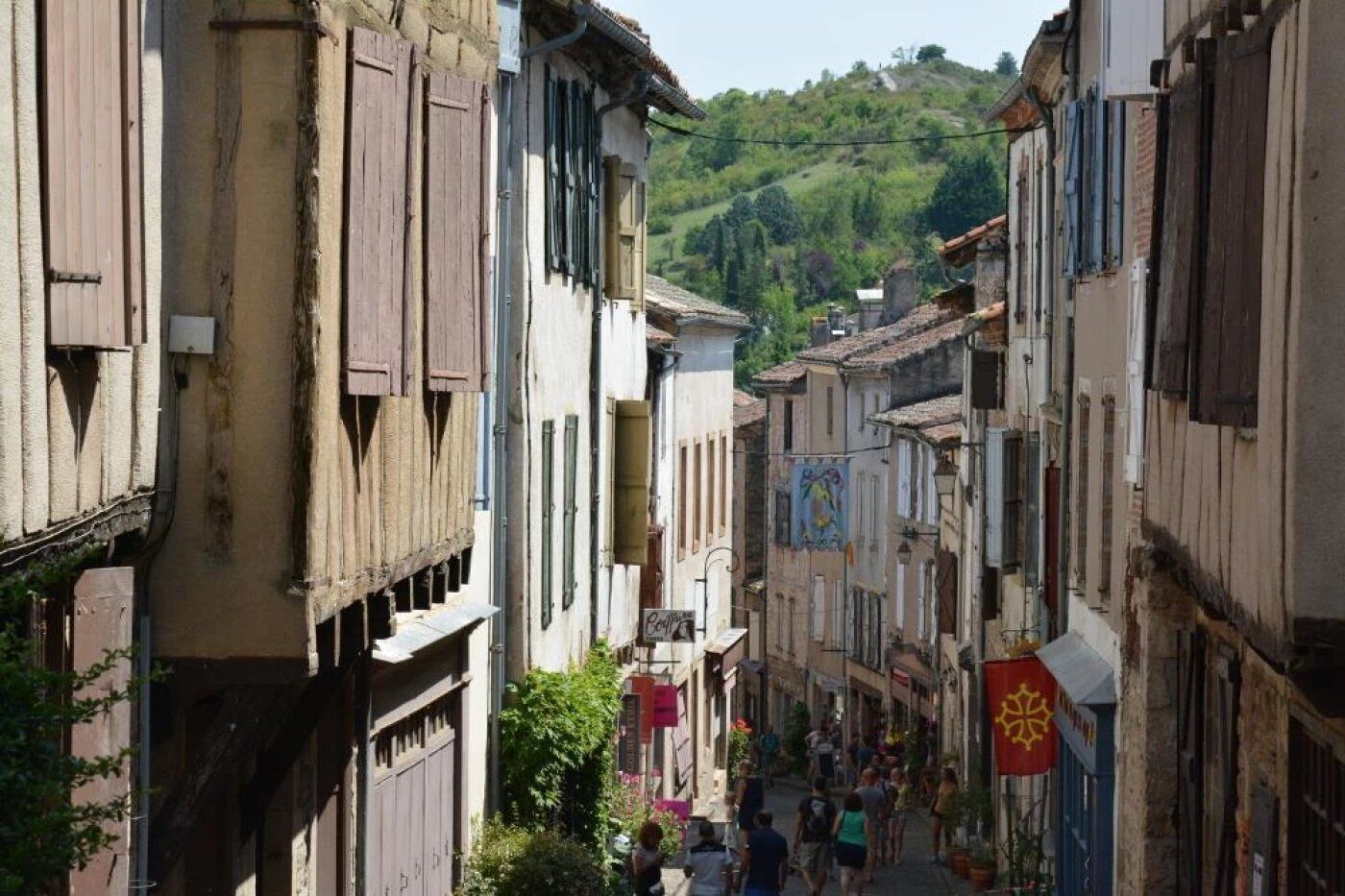 A narrow street lined with traditional buildings, some with wooden shutters, and a few with colorful decorations.