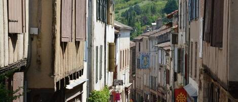 A narrow street lined with traditional buildings, some with wooden shutters, and a few with colorful decorations.