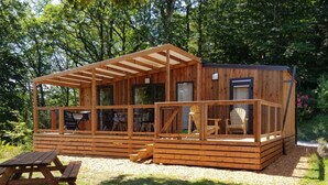 Una cabaña de madera con un porche cubierto, una mesa de picnic y un perro acostado sobre el césped.
