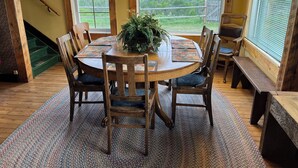 A round wooden dining table with a central plant, surrounded by six chairs with cushioned seats. - Quaint lodge wonderful for retreats, reunions, weddings, and relaxation! (Glenwood)