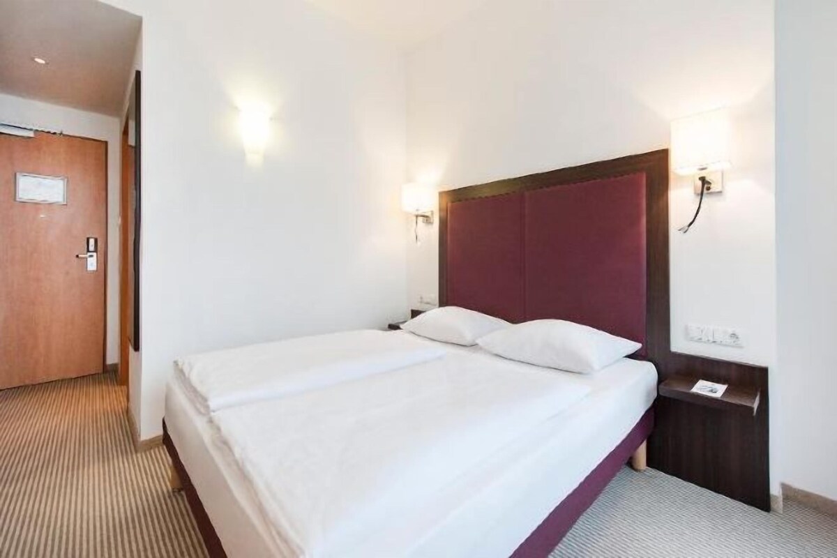 Habitación de hotel con una cama individual, cabecera de madera, mesita de noche y lámpara fijada a la pared.