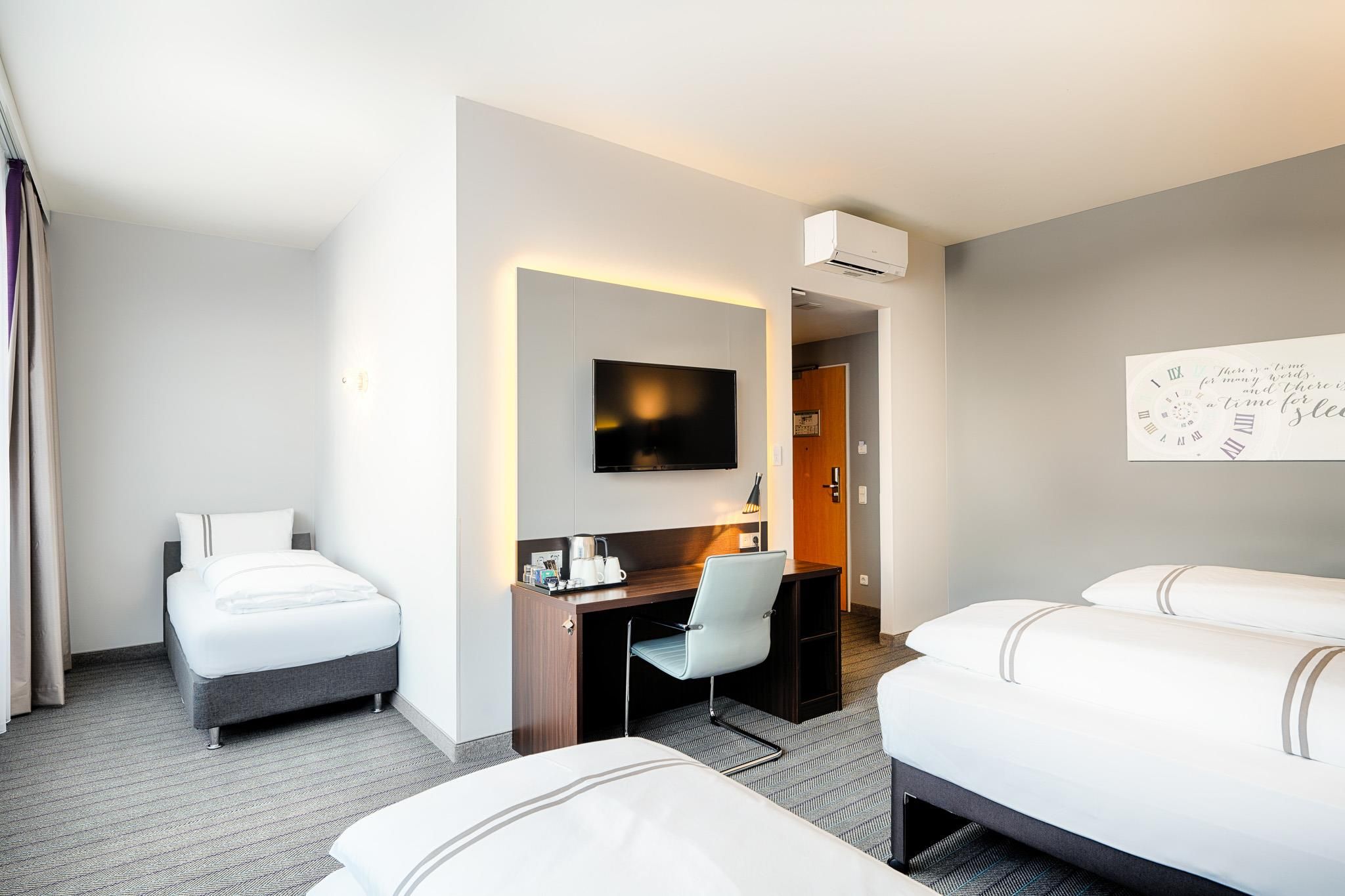 Habitación de hotel con dos camas, un escritorio, una silla, un televisor y un equipo de aire acondicionado.