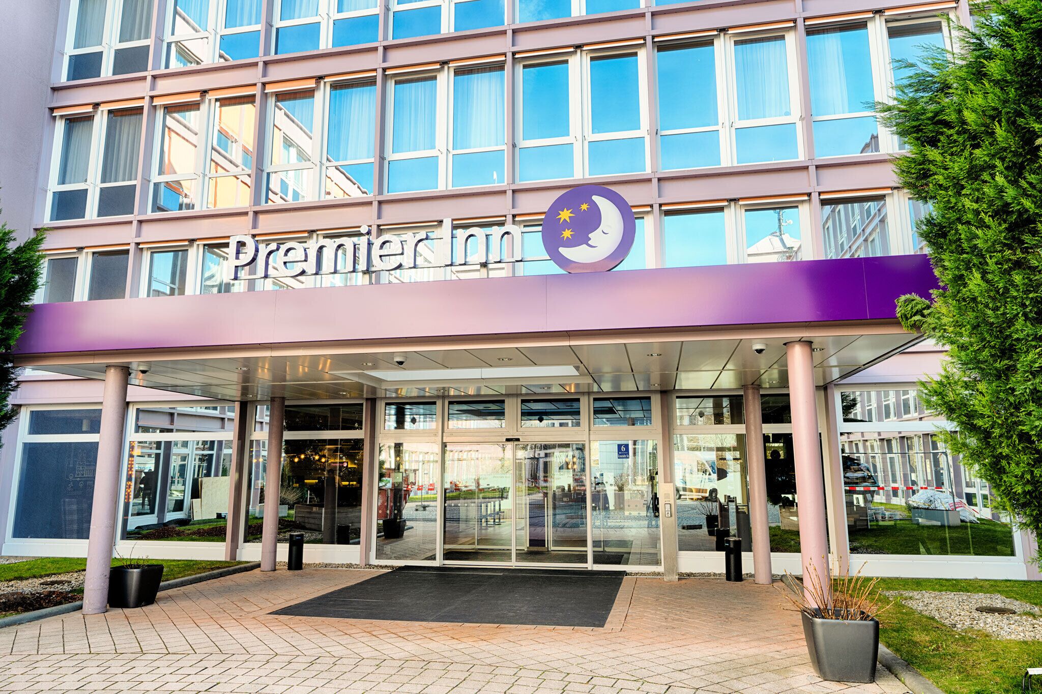 A hotel entrance with a glass facade, a purple awning, and a logo with a crescent moon and stars.