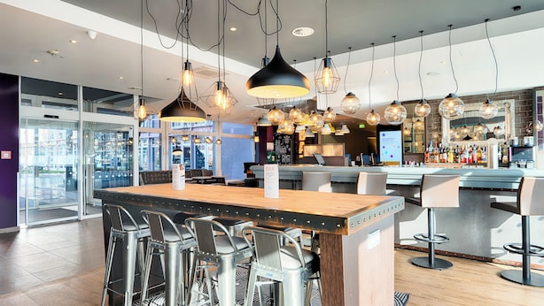 A modern bar area with a central island, bar stools, hanging pendant lights, and a bar counter with a variety of bottles.
