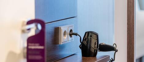 A hairdryer plugged into a wall socket on a wooden shelf.