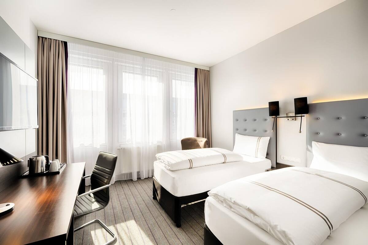 Habitación de hotel con cama, escritorio, silla, televisión y ventana con cortinas.